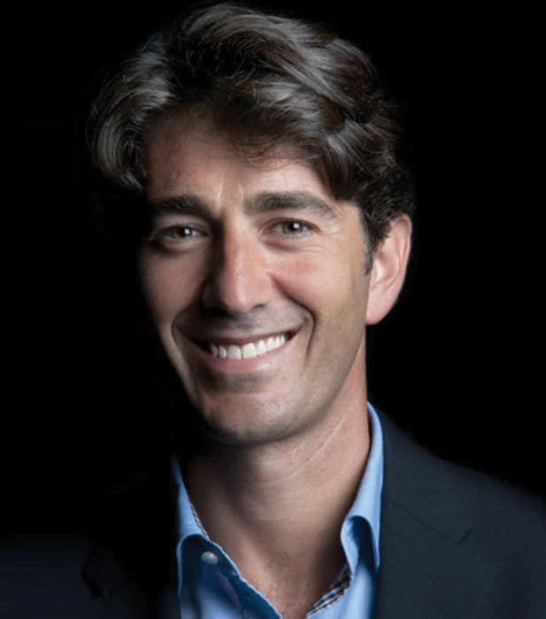 Ritratto di Dr. Antonello Melis, medico sorridente con camicia azzurra e giacca scura.